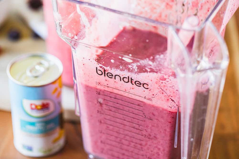 Blender cup is full of vibrant purple Mixed Berry Pineapple Smoothie ready to serve.