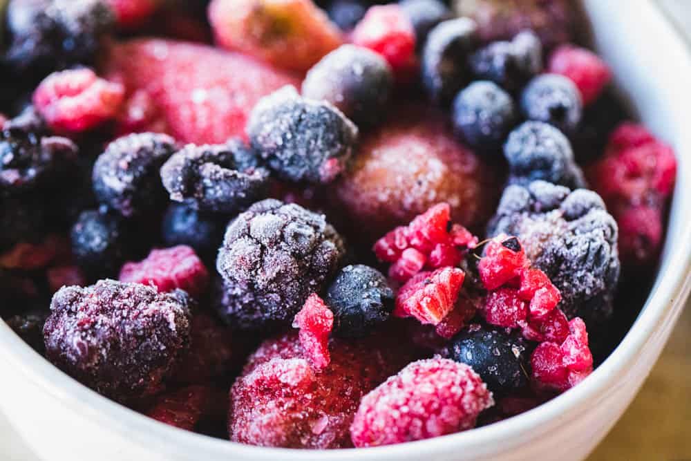 Frozen blackberries, blueberries, raspberries and strawberries sit in a white ceramic bowl.