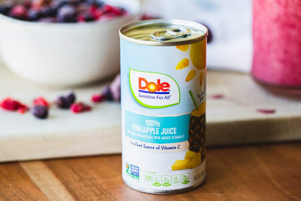 Small personal size can of pineapple juice sits on a counter with other ingredients for the smoothie behind.