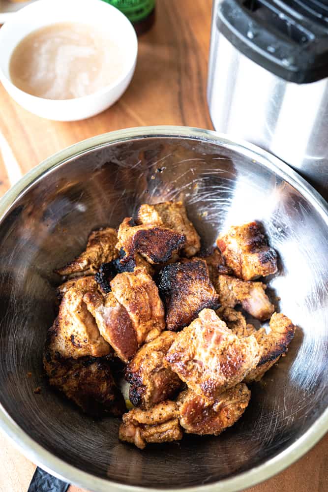 Seared cuts of seasoned pork sit in a metal bowl to cool off.