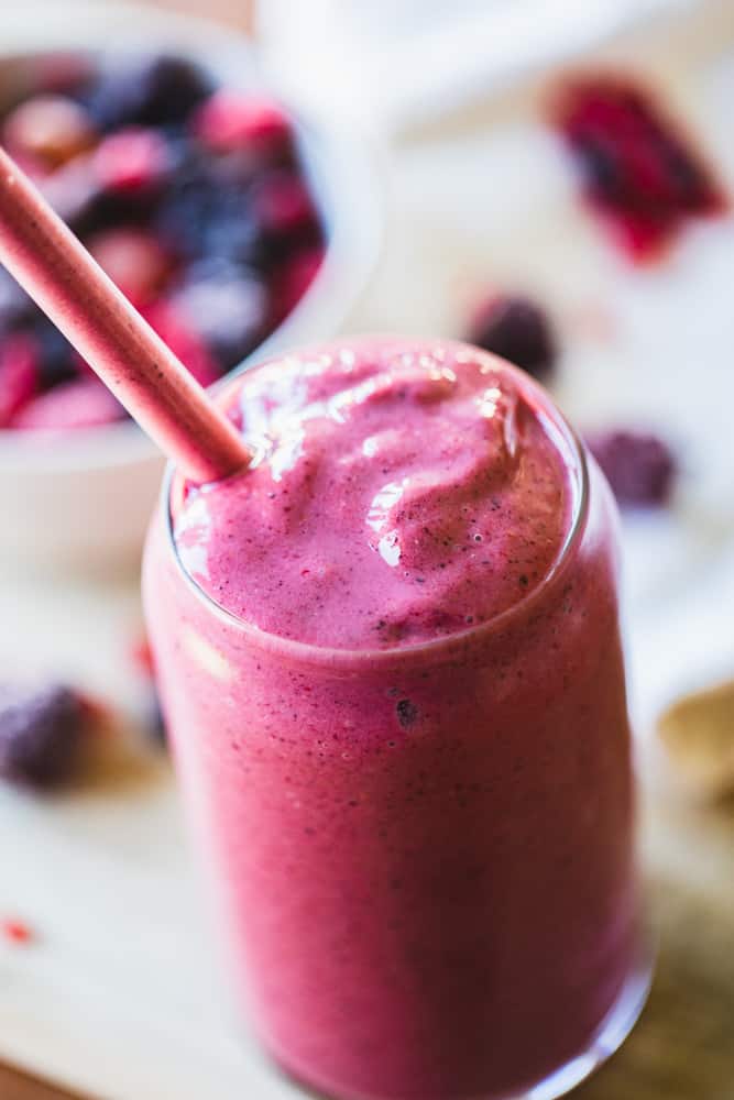 Rich purple berry pineapple smoothie sits in a glass with straw.