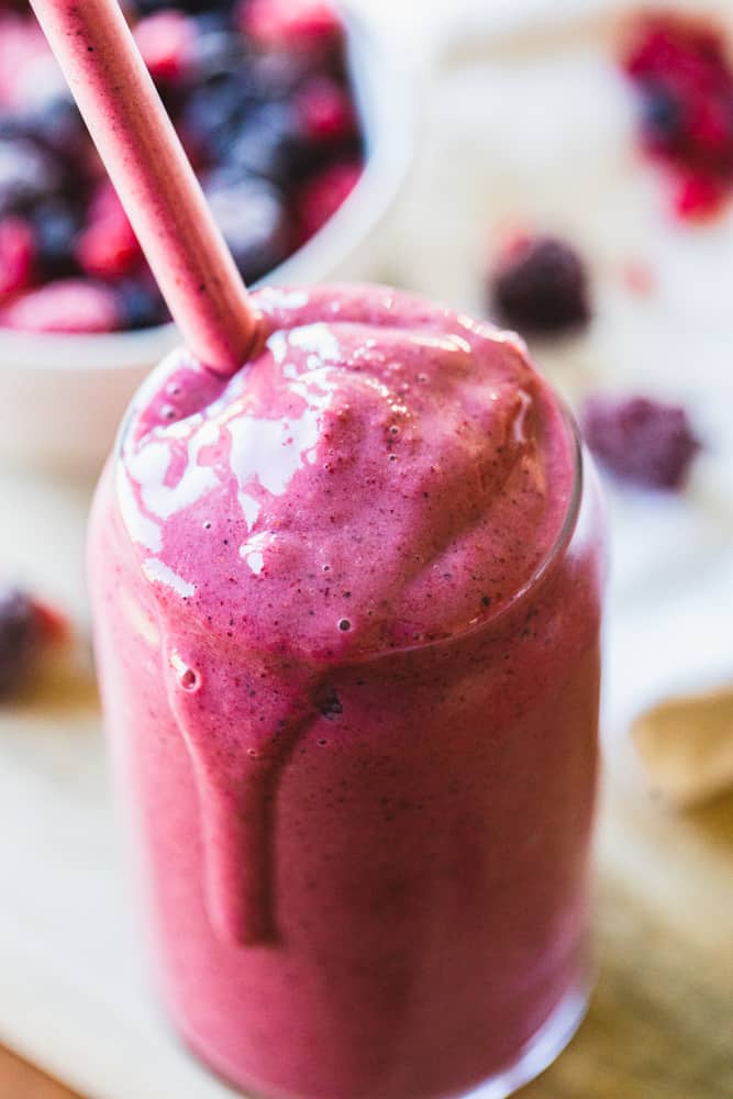 A tall glass filled with Mixed Berry Pineapple smoothie overflows ready to be enjoyed!