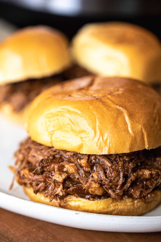 Three pulled pork sandwiches sit on a white plate for serving.