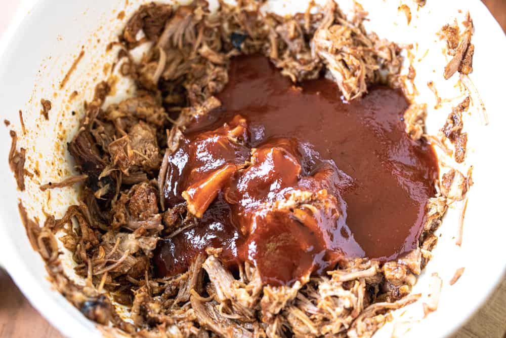 Shredded pulled pork sits in a bowl with barbecue sauce poured over the meat.