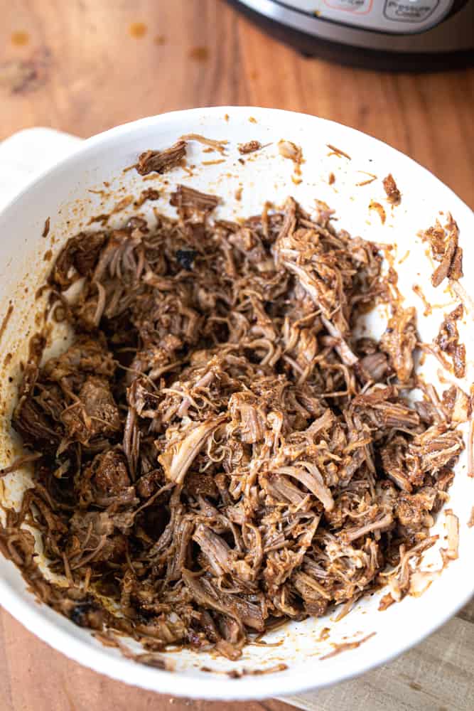 Cooked pork is shredded and sits in a white bowl.