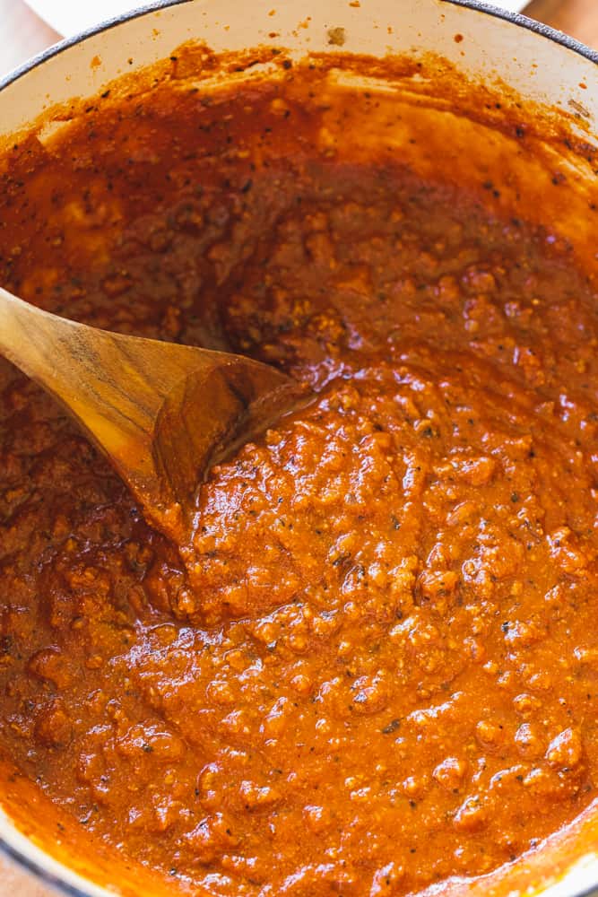 Wooden spoon stirs large pot of spaghetti sauce.