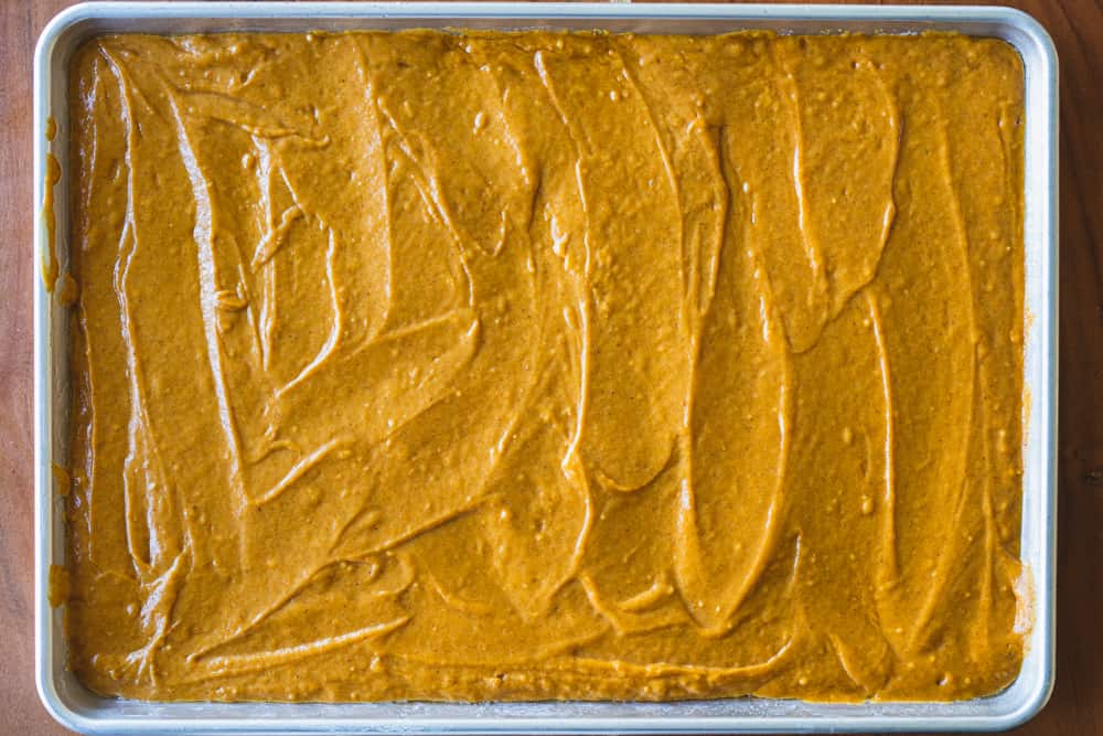 Cake batter is spread out evenly in a large jelly pan for baking.