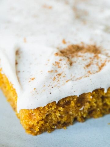 Frosted slice of pumpkin sheet cake sits on plate ready to be enjoyed.