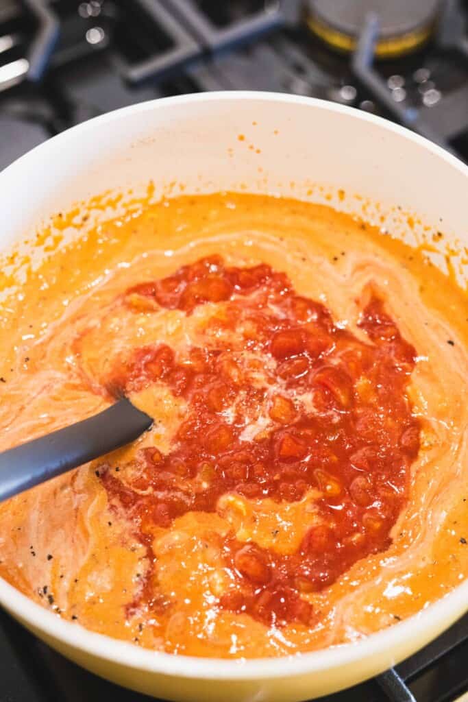 Tomato soup base sits in a large pot on the stove. A can of diced tomatoes sits over the top to be stirred in.