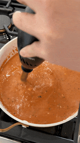 Ashley holds an immersion blender and purees creamy tomato soup ingredients in a large pot.