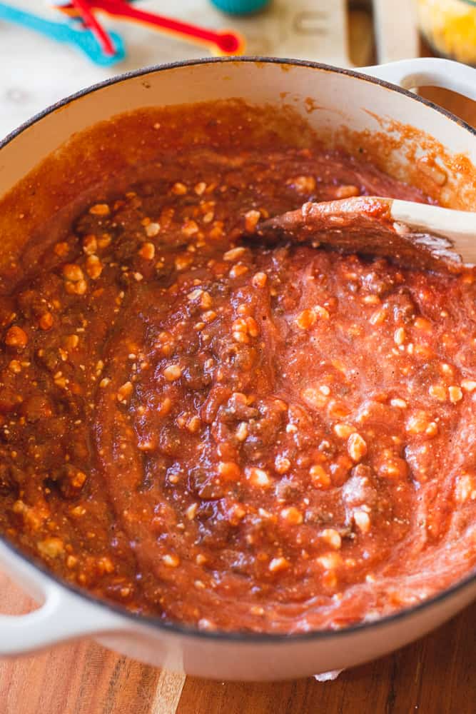 Wooden spoon stirs pot of prepared meat sauce for lasagna.