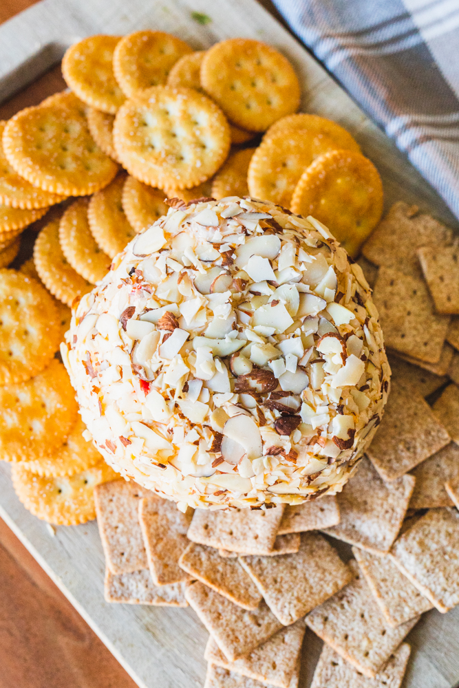 Holiday cheese ball sits on a wooden serving tray surrounded by crackers for dipping.