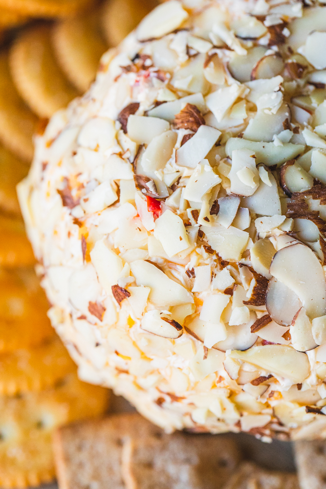 Cheese ball rolled in sliced almonds is surrounded by an assortment of crackers.