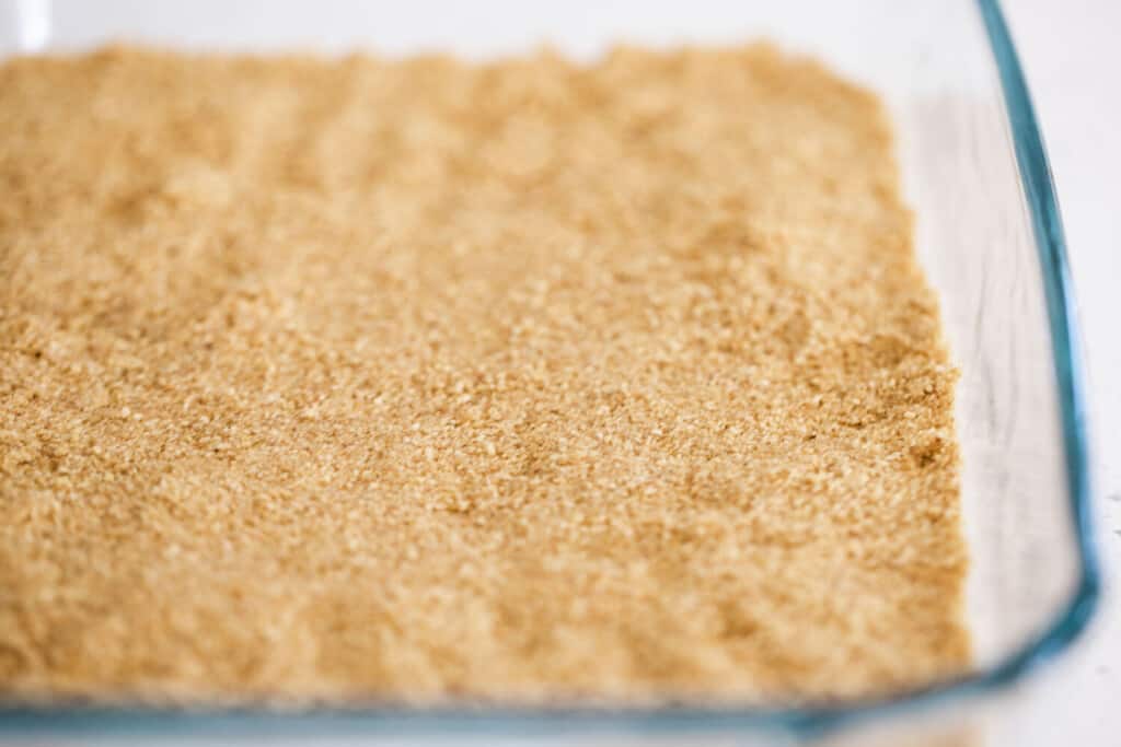 Graham cracker crumb crust is pressed into the bottom of a glass baking dish.