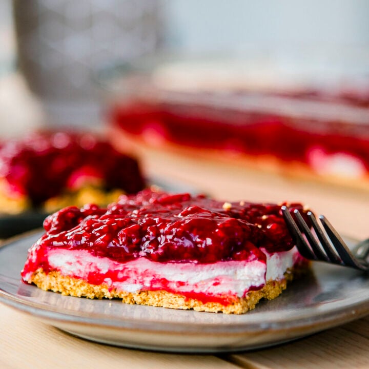Slice of No Bake Raspberry Cheesecake Bars sits on a plate beside a fork.