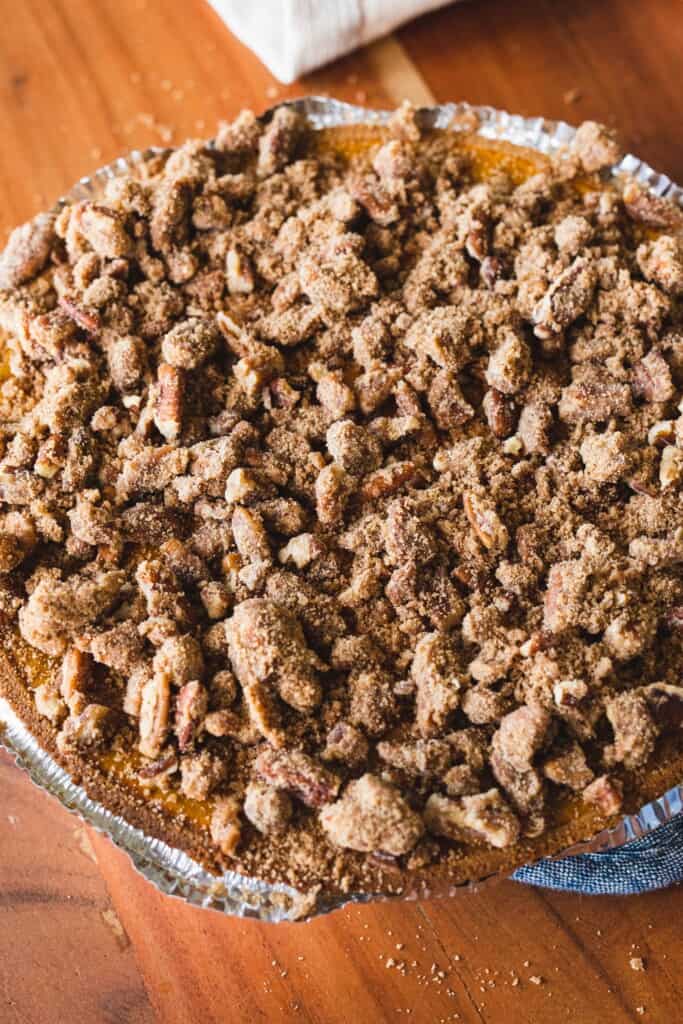 Pumpkin pie topped with pecan streusel sits on the counter ready to go in the oven.
