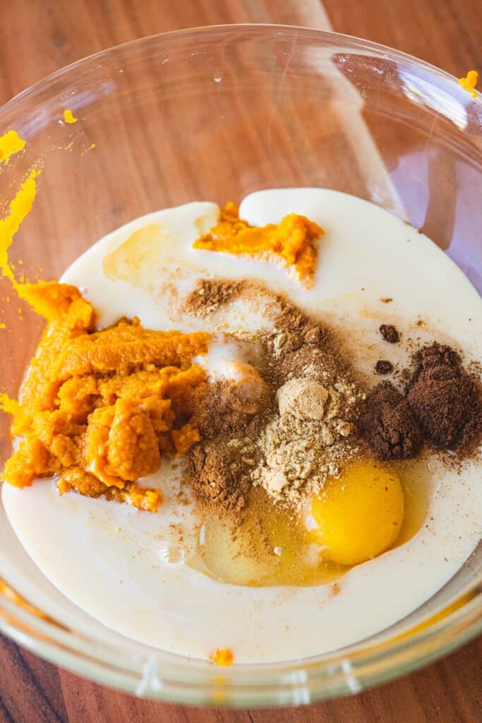 Pumpkin, condensed milk, spices and an egg sit in a glass bowl.