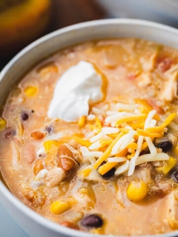 Bowl of creamy taco soup sits in a white bowl topped with shredded cheese and dollop of sour cream.