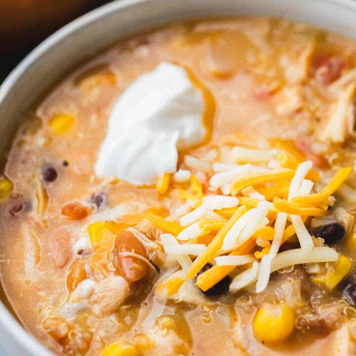 Bowl of creamy taco soup sits in a white bowl topped with shredded cheese and dollop of sour cream.