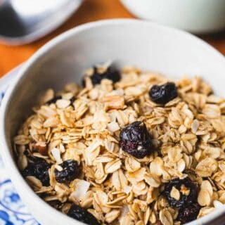 A white bowl filled with granola sits on a blue plate.