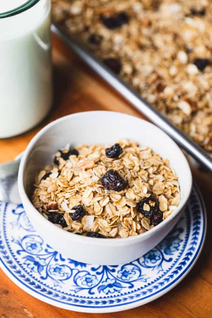A bowl of baked rolled oats and craisins, coconut and pecans sits on a blue decorative plate.