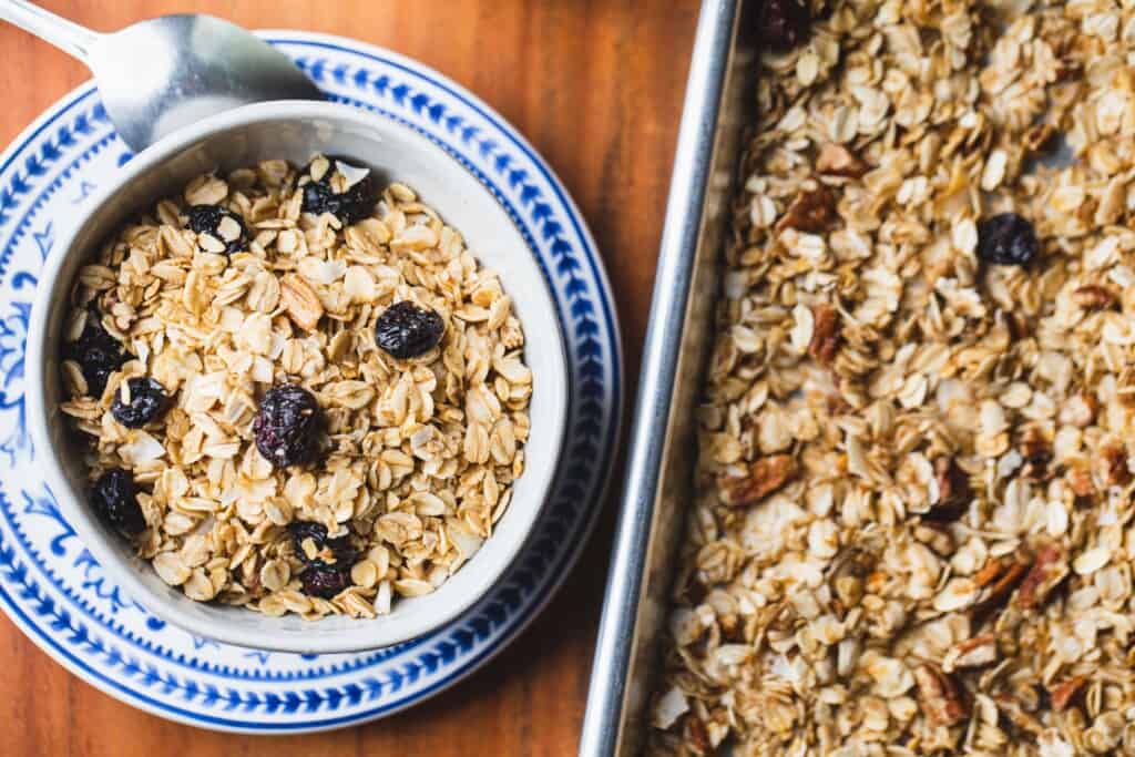 Bowl of granola sits on a plate beside a tray of baked goodness.