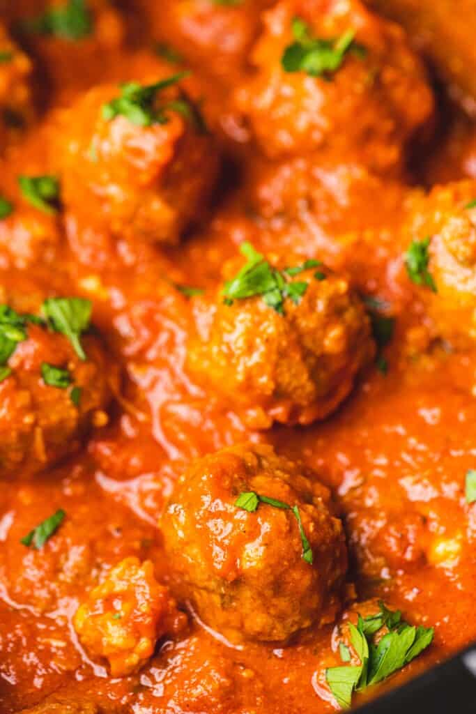 Stuffed meatballs sit in tomato sauce and topped with fresh basil.