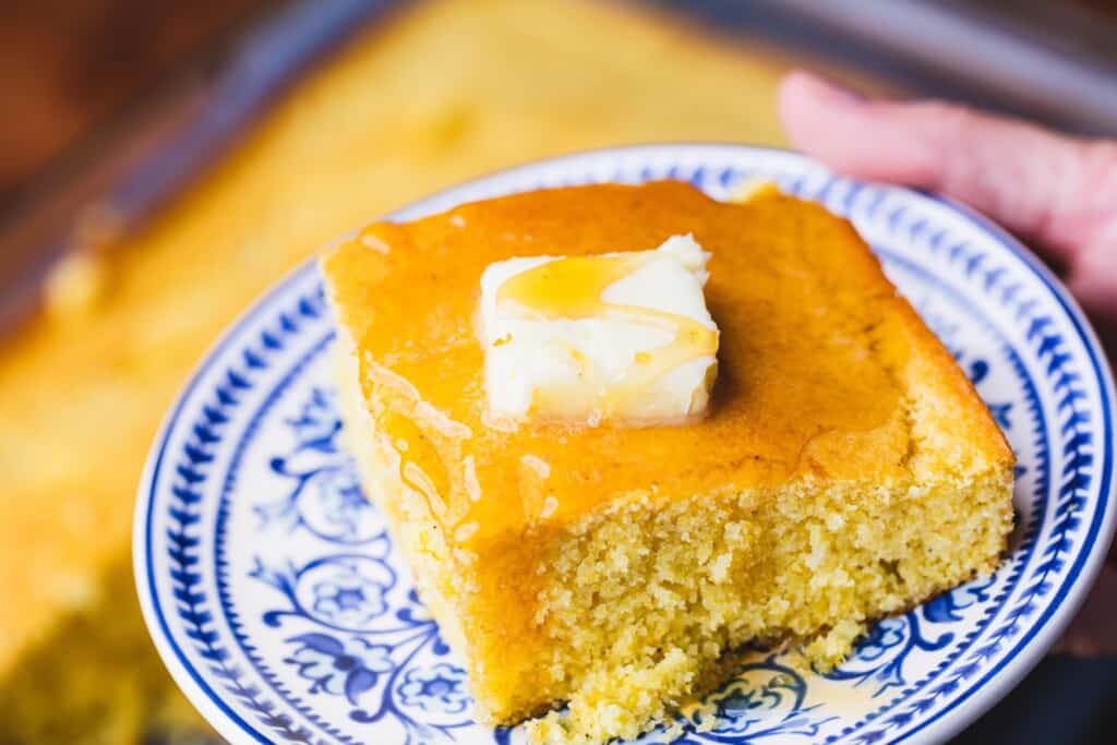 Slice of sweet cornbread sits on a decorative blue and white plate for serving.