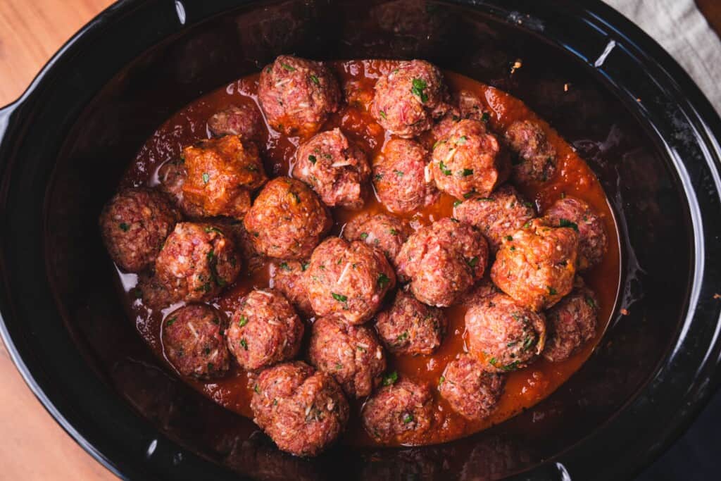 Raw meatballs sit in a slow cooker filled with red tomato sauce.
