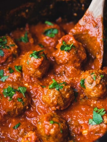 Cooked mozzarella stuffed meatballs sit in a slow cooker ready to serve.