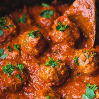 Cooked mozzarella stuffed meatballs sit in a slow cooker ready to serve.