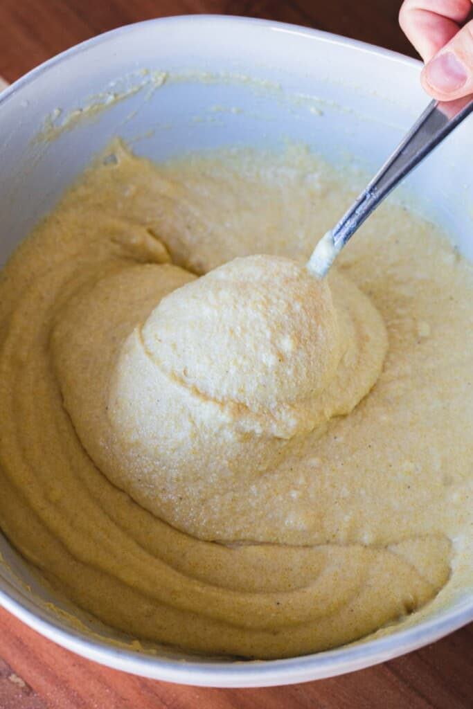 Smooth cornbread batter is stirred with metal spoon.