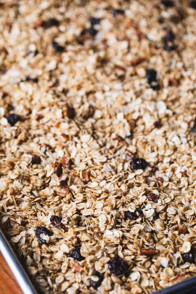 Granola is spread thinly out across a baking sheet.