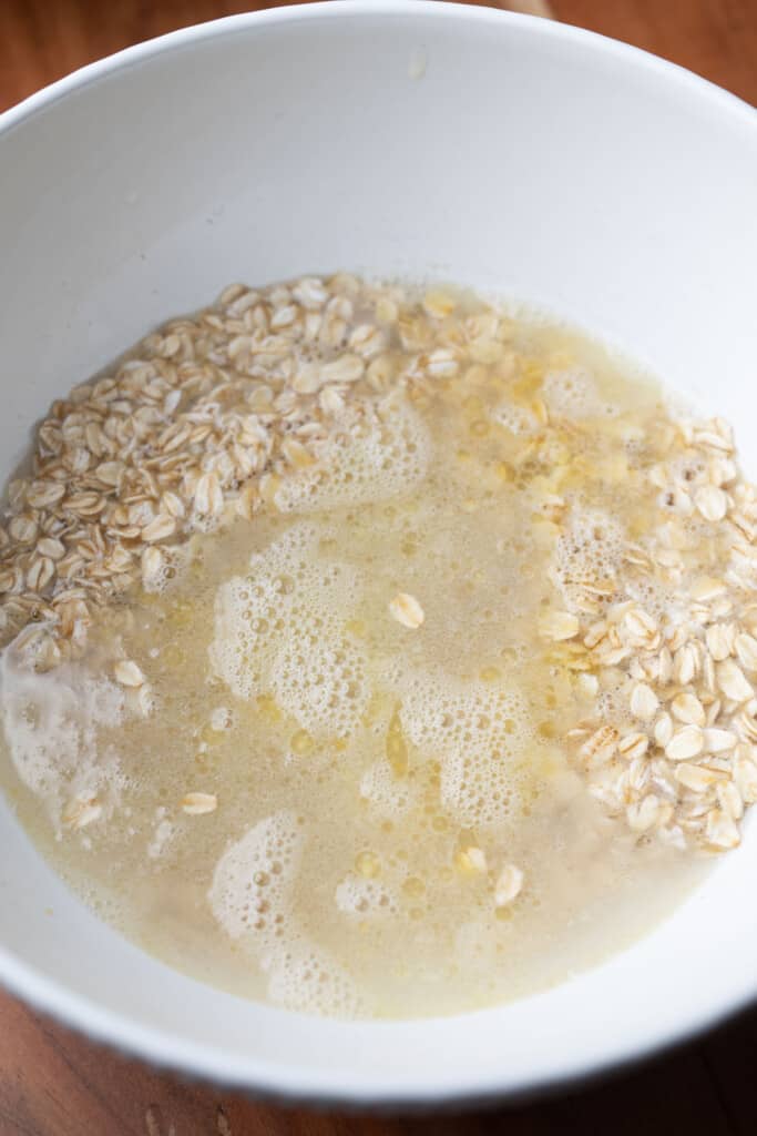 Old fashioned rolled oats sit in a bowl with butter and hot water soaking.