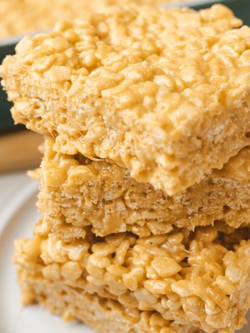 Bars of Caramel Rice Krispie Treats are stacked on a white plate four high.
