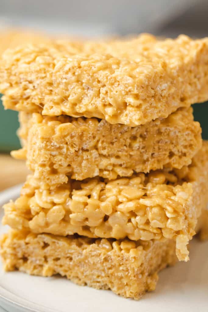 Four bars of Caramel Rice Krispie Treats are stacked on top of each other on a plate.