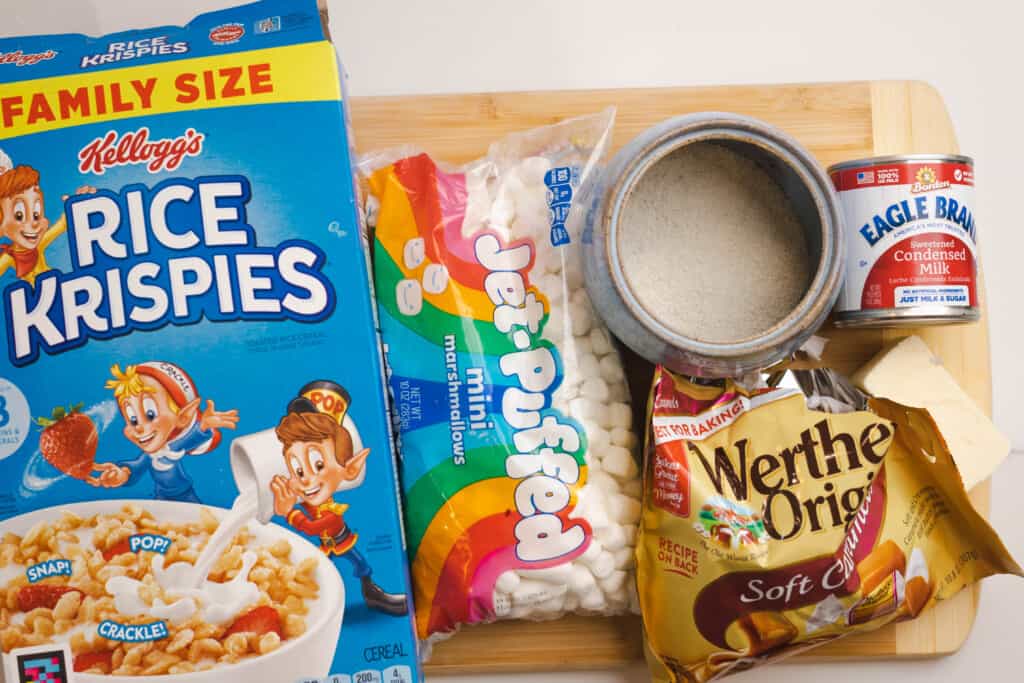 Ingredients for caramel rice krispie treats sit on a wooden cutting board ready to be combined.
