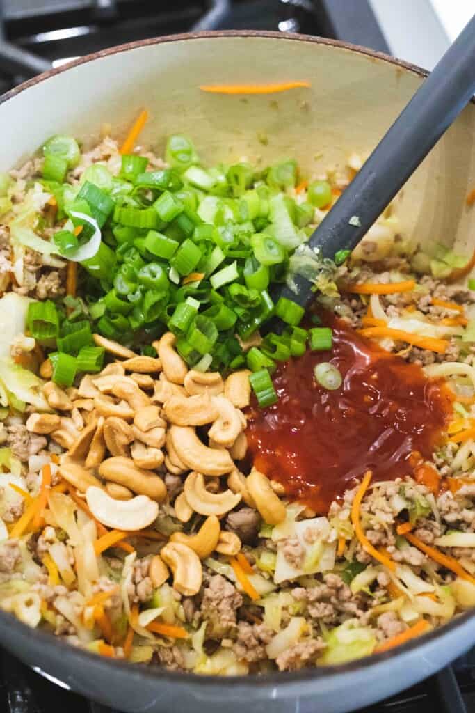 Green onion, cashews, sweet and sour sauce are added to the pot of cooked ground pork, and other ingredients.