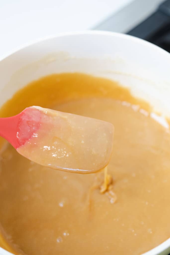 Melted sweet caramel sauce sits in a pot on the stove with a red spatula.