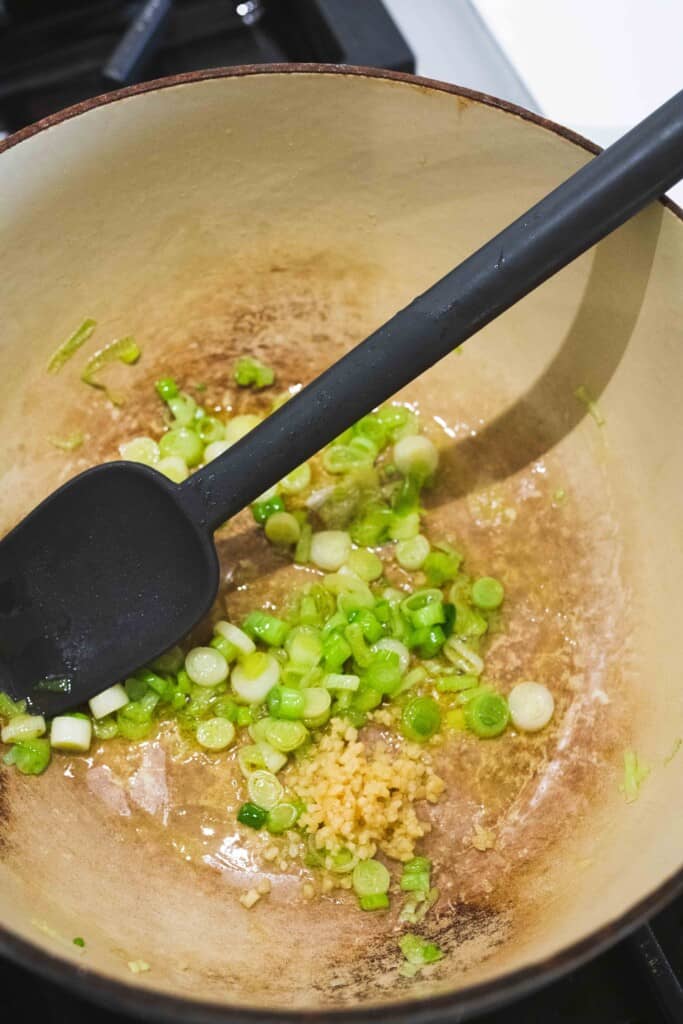 Green onion and minced garlic sit in a large pot with olive oil over the stove to be sauted.