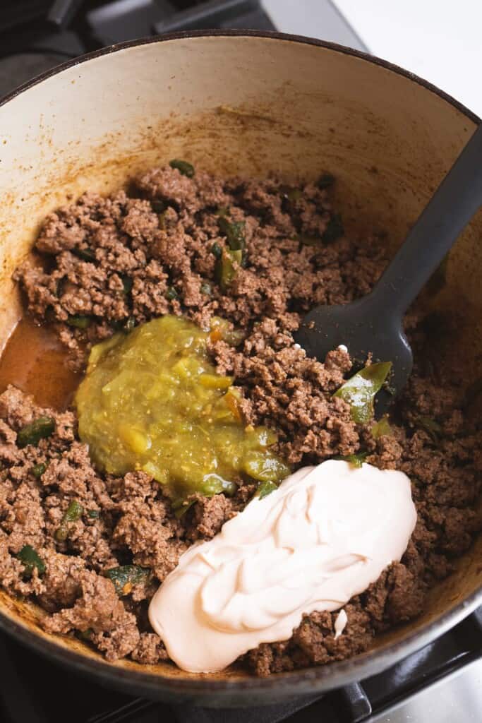 Cooked grown beef, salsa, crema, seasonings and peppers sit in a pot ready to be mixed together.