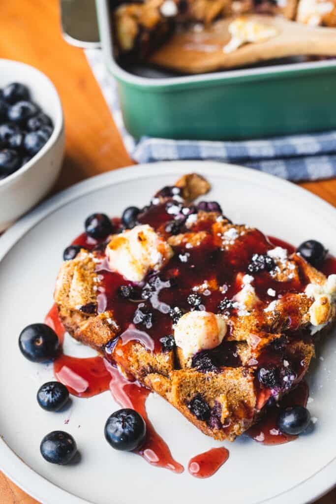 Topped with syrup a serving of French Toast Bake breakfast casserole sits on a small white plate for eating.