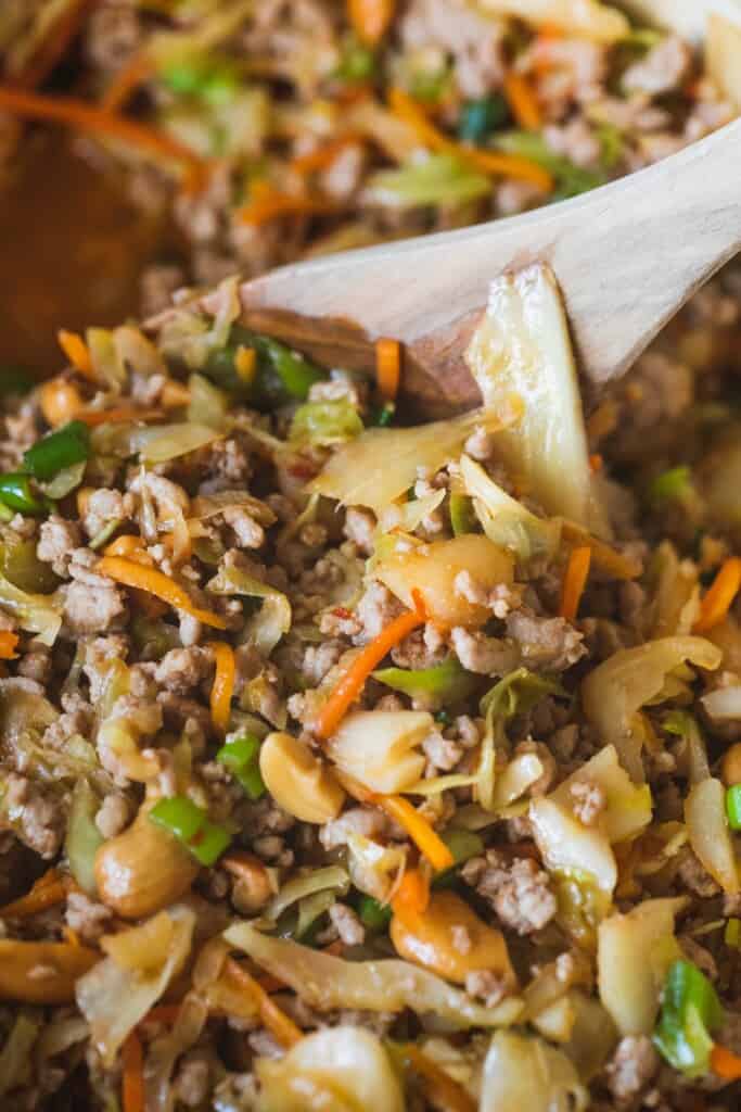 A wooden spoon stirs egg roll in a bowl filling, mixing everything together.