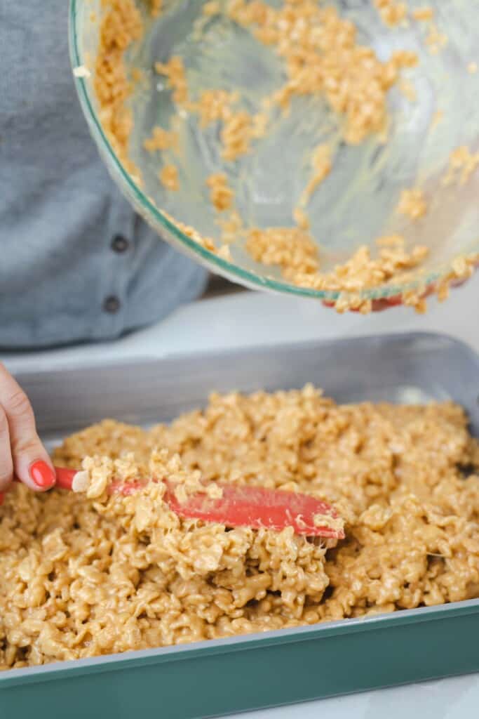 A spatula spreads out the cereal treat mixture into a dish.