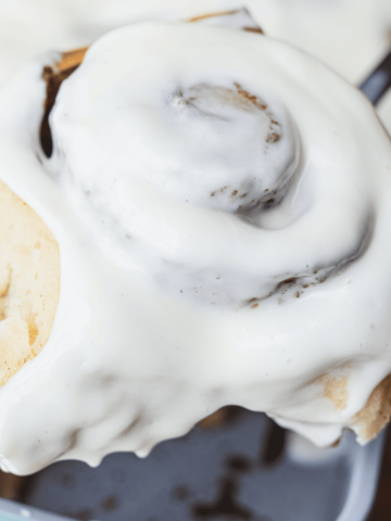 A spatula holds a large iced cinnamon roll after lifting out of a baking dish.