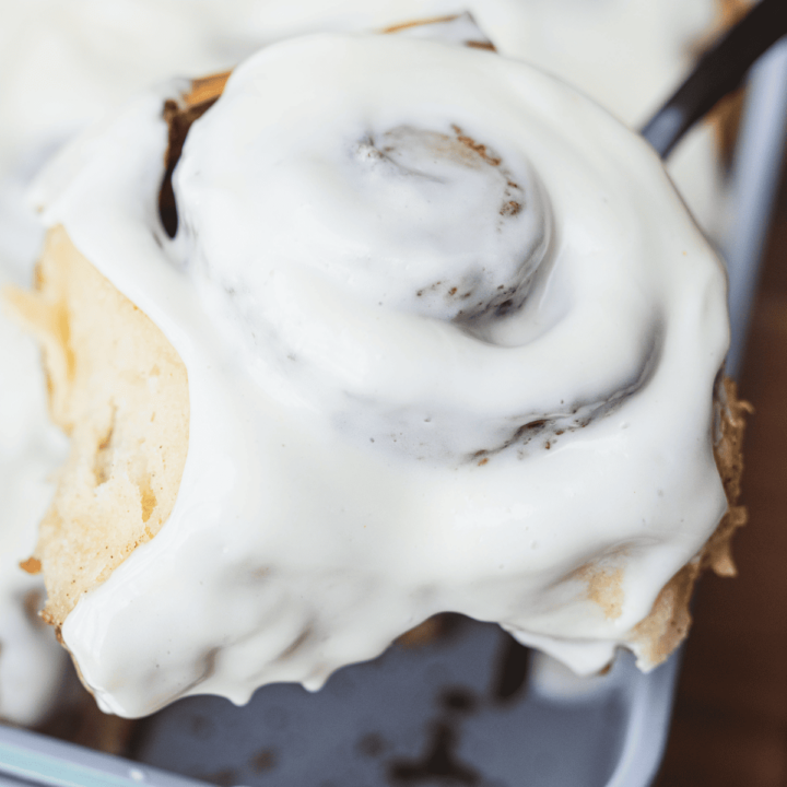 A spatula holds a large iced cinnamon roll after lifting out of a baking dish.