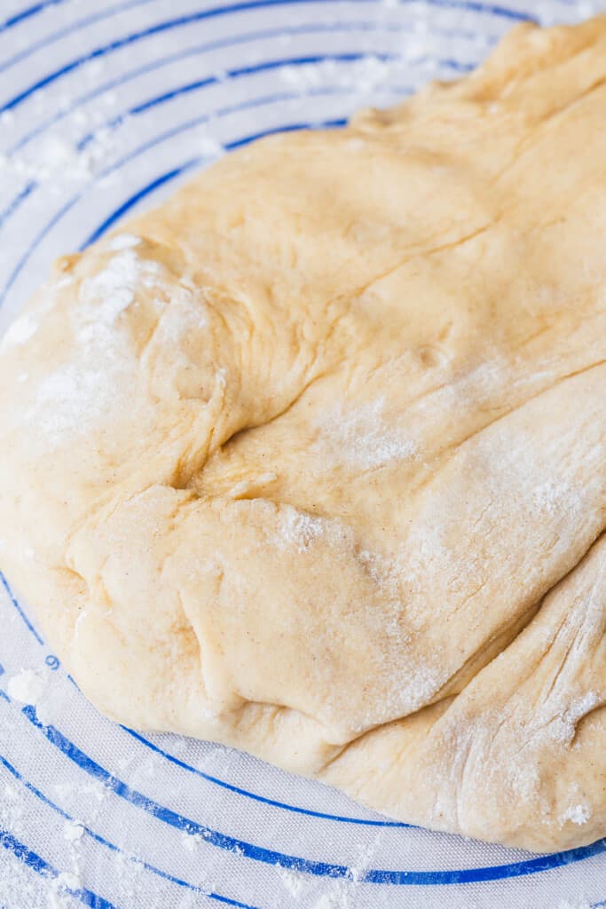 Prepared sweet dough for cinnamon rolls sits on a pastry mat with a dusting of flour.