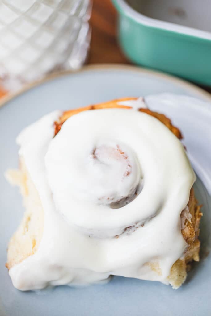 A large cinnamon roll sits on a plate topped with icing