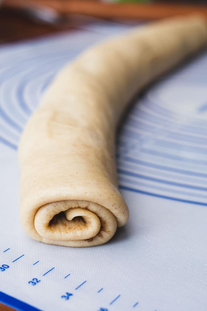 Sweet roll dough topped with filling is rolled into a log shape ready for cutting.