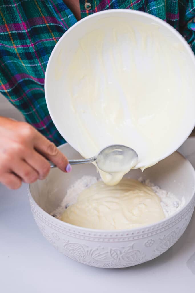 Wet ingredients are spooned into the bowl of dry ingredients for the cake.